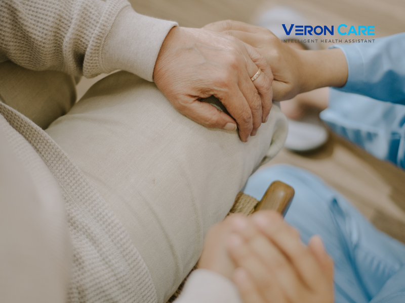Caregiver gently holding an elderly person’s hand while providing support, with Veron Care logo in the corner.”